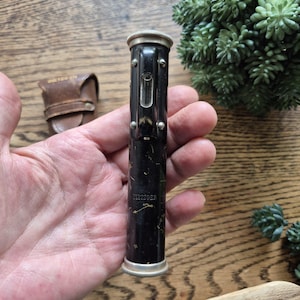 May include: A vintage black cylindrical Dietzgen drafting tool with a silver-toned metal cap and base, featuring a small glass level vial mounted on the side with four screws. The black finish shows signs of wear and the brand name Dietzgen is visible.
