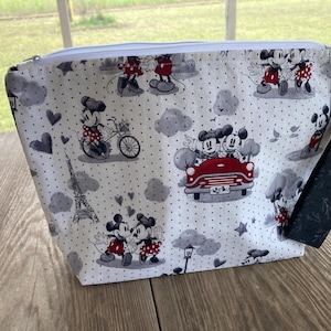 May include: A white zippered pouch with a black and white polka dot pattern featuring Mickey Mouse and Minnie Mouse in various scenes. The pouch has a black zipper and a black strap.