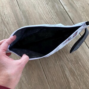 May include: White zippered pouch with a black lining and a black zipper pull. The pouch is open and the lining is visible.