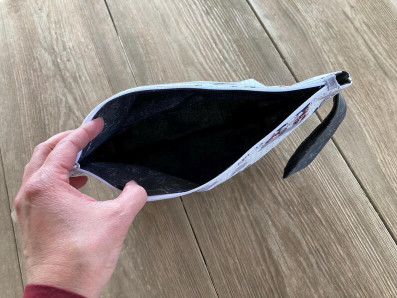 May include: White zippered pouch with a black lining and a black zipper pull. The pouch is open and the lining is visible.