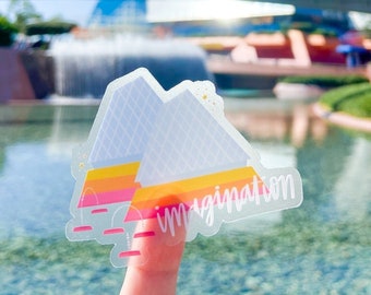 Könnte beinhalten: Ein transparenter Aufkleber mit einem pinkfarbenen, gelben und orangenen Design der Spaceship Earth-Attraktion in Epcot. Der Aufkleber trägt die Aufschrift "imagination" in weißen Buchstaben.