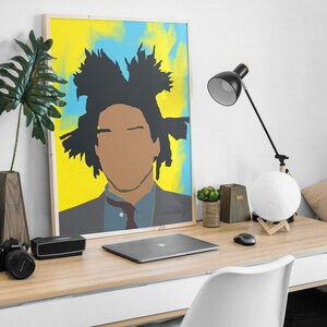 May include: A framed poster featuring a colourful abstract portrait of a person with a black afro. The poster is hanging on a white wall above a wooden desk with a laptop, a lamp, and a potted plant.