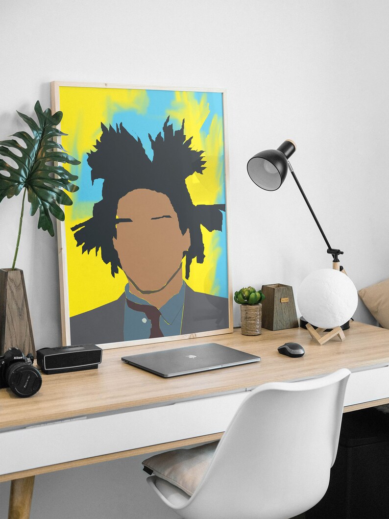 May include: A framed poster featuring a colourful abstract portrait of a person with a black afro. The poster is hanging on a white wall above a wooden desk with a laptop, a lamp, and a potted plant.