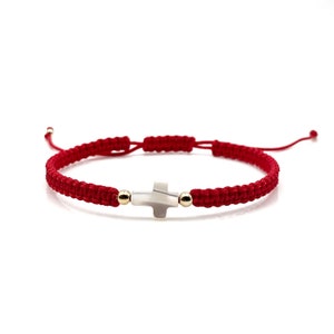 May include: Red string bracelet with a silver cross charm and gold beads.