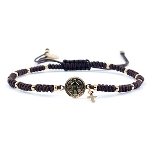 May include: A brown cord bracelet with a gold Saint Christopher medal and a small gold cross charm.