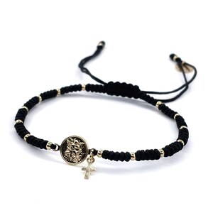 May include: Black braided bracelet with a gold charm featuring a religious icon and a small cross.