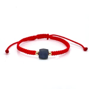 May include: A red string bracelet with a dark blue square bead and gold accents.