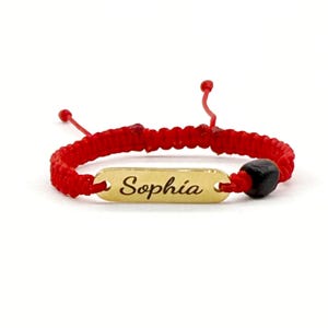 May include: Red string bracelet with a gold nameplate that says "Sophia" and a black bead.