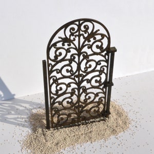 Puede incluir: Una puerta de metal decorativa con un dise&ntilde;o de desplazamiento. La puerta est&aacute; hecha de metal negro y tiene una p&aacute;tina marr&oacute;n. La puerta est&aacute; de pie sobre una superficie blanca.