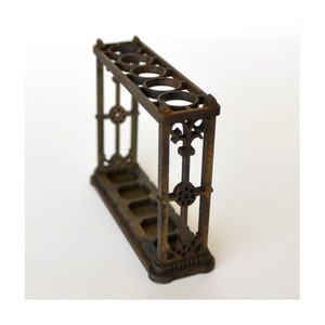 Puede incluir: Un soporte para paraguas vintage de metal adornado con cinco ranuras. El soporte está hecho de metal oscuro oxidado y tiene un diseño decorativo.