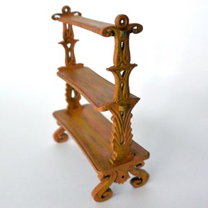 May include: A small, wooden shelf unit with three shelves and ornate, carved details. The shelf is painted in a distressed, brown finish.