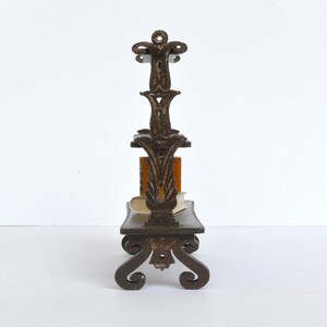 May include: A dark brown metal bookshelf with ornate scrollwork and three shelves. The bookshelf is designed to hold small books or other decorative items.