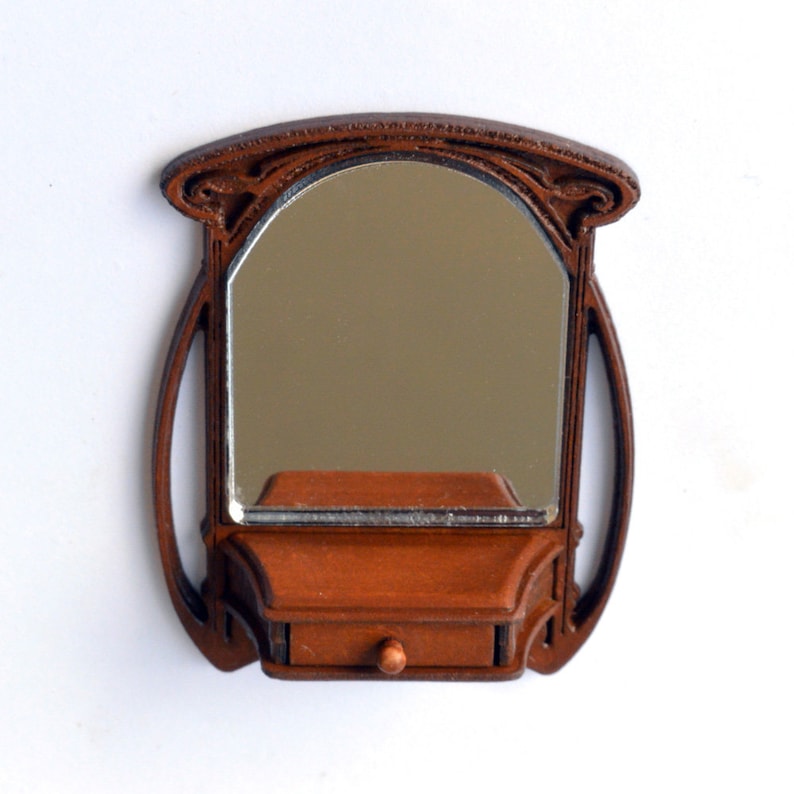 May include: A brown wooden wall-mounted mirror with an arched top and a small shelf with a drawer below. The mirror has a decorative design around the frame.