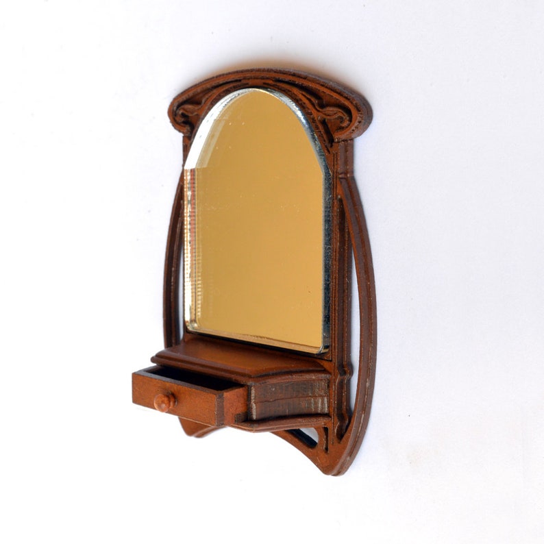 May include: A wooden wall-mounted mirror with an arched top and a small drawer below. The mirror has a brown finish and a gold-colored reflection.