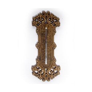 Op de afbeelding: Houten thermometer met een sierlijk, krullend ontwerp. De thermometer heeft een bruine afwerking en een zilveren temperatuurmeter. De temperatuurschaal is in Celsius. De thermometer is ontworpen met een decoratieve boven- en onderkant.