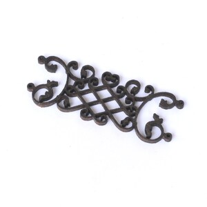 Puede incluir: Un adorno decorativo de madera marr&oacute;n oscuro con un dise&ntilde;o intrincado y ornamentado. El dise&ntilde;o presenta un patr&oacute;n repetitivo de espirales y bucles, creando una apariencia delicada y elegante.