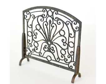 May include: A black metal fireplace screen with a decorative, ornate design. The screen has a curved top and stands on four legs.