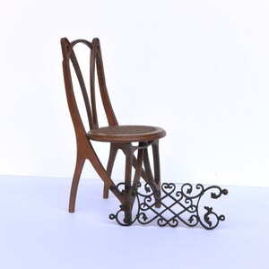 Puede incluir: Una silla de madera con un dise&ntilde;o &uacute;nico y una valla de metal decorativa. La silla tiene un respaldo curvo y un asiento tejido. La valla es de metal negro y tiene un patr&oacute;n decorativo.