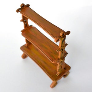 May include: A three-tiered wooden shelf with ornate carvings. The shelf is painted in a warm brown color with a distressed finish.
