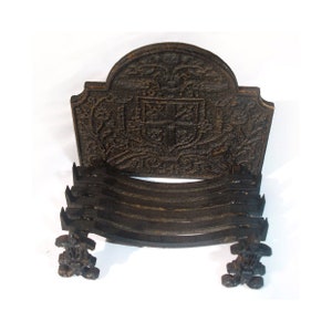 Peut inclure: Un foyer en fonte noire avec un dessus décoratif orné d'un motif floral et d'un bouclier. La grille est composée de plusieurs barres courbes et possède des pieds décoratifs.