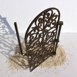 Puede incluir: Una puerta de metal decorativa con un dise&ntilde;o detallado e intrincado. La puerta est&aacute; hecha de metal marr&oacute;n y tiene un aspecto r&uacute;stico y envejecido. La puerta est&aacute; tumbada sobre una superficie blanca.