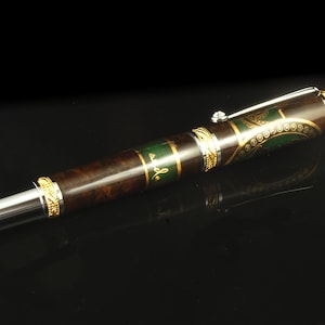 May include: A brown and green pen with gold accents and a silver clip. The pen has a decorative design on the barrel.