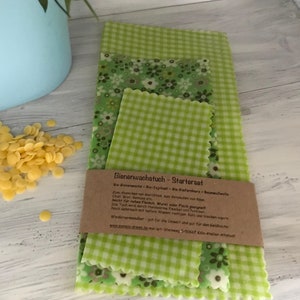 Könnte beinhalten: Ein Set mit drei grünen und weißen gemusterten Bienenwachstüchern. Die Tücher sind aus Baumwolle und Bienenwachs und wiederverwendbar. Der Text auf der Verpackung lautet "Bienenwachstuch - Starterset".