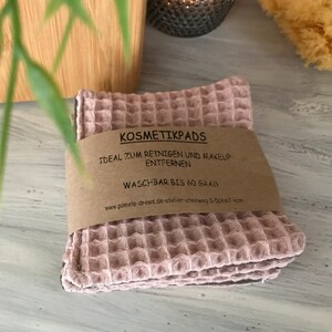 Könnte beinhalten: Ein Stapel rosa, gewellte, wiederverwendbare Abschminkpads mit einem braunen Papieraufkleber, auf dem steht: "KOSMETIKPADS IDEAL ZUM REINIGEN UND MAKEUP ENTFERNEN WASCHBAR BIS 60 GRAD www.pamela-drews.de-atelier-steinweg 5-50667 Koln".