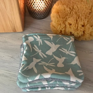 Könnte beinhalten: Ein Stapel aus vier wiederverwendbaren Abschminkpads in Tealblau mit einem weißen Kolibri- und Libellenmuster. Die Pads bestehen aus weichem, saugfähigem Stoff.