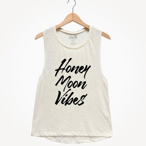Puede incluir: Un top blanco sin mangas con el texto "Honey Moon Vibes" impreso en negro.