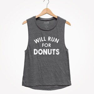 Könnte beinhalten: Dunkelgraues Muskel-Tanktop mit dem weißen Aufdruck „WILL RUN FOR DONUTS“. Das ärmellose Oberteil hängt an einem Holzbügel vor weißem Hintergrund.
