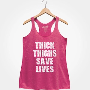 May include: Pink racerback tank top with the text "THICK THIGHS SAVE LIVES" in white distressed lettering.