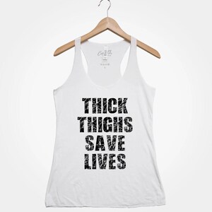 May include: White tank top with a black graphic that says "Thick Thighs Save Lives".