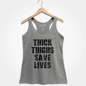 May include: Gray tank top with the text "THICK THIGHS SAVE LIVES" printed in black.