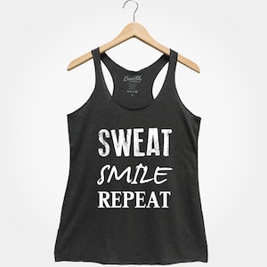以下が含まれることがあります： 暗いグレーのタンクトップに「SWEAT SMILE REPEAT」という白い文字が書かれています。文字は、使い古したようなヴィンテージ風です。