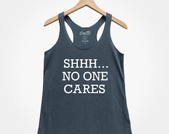 May include: A dark gray tank top with the text "SHHH... NO ONE CARES" printed in white.