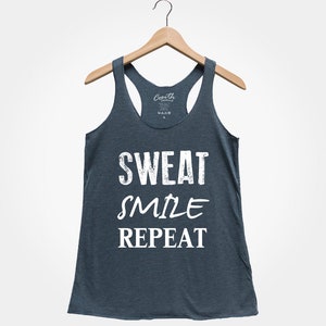 May include: A dark blue tank top with the text "SWEAT SMILE REPEAT" in white. The tank top is hanging on a wooden hanger.