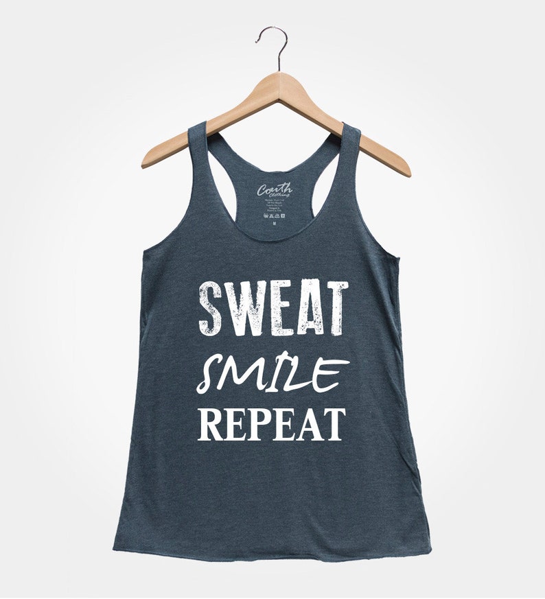 May include: A dark blue tank top with the text "SWEAT SMILE REPEAT" in white. The tank top is hanging on a wooden hanger.