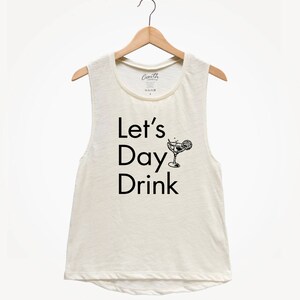 May include: A white sleeveless tank top with the text "Let's Day Drink" and a black and white illustration of a cocktail glass with a lemon wedge.