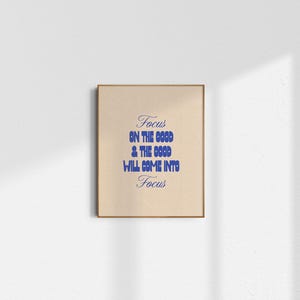 May include: A beige printable wall art print with a blue text overlay that reads "Focus on the good & the good will come into focus".