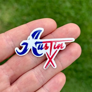 May include: A sticker with the word "Austin" in a stylized design. The letter "A" is blue with a white star, the "us" is blue, and the "tin" is red. A red "X" is below the word.