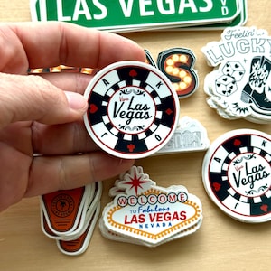 May include: A collection of Las Vegas-themed stickers. One sticker is a casino chip design with the words "Viva Las Vegas". Other stickers include a "Welcome to Fabulous Las Vegas Nevada" sign, dice, and a cowboy boot.