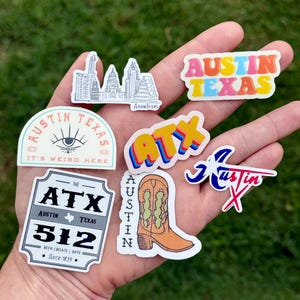 May include: A collection of colorful stickers featuring designs related to Austin, Texas. Designs include the city skyline, the text "Austin Texas" in various fonts, a cowboy boot, and the area code 512.