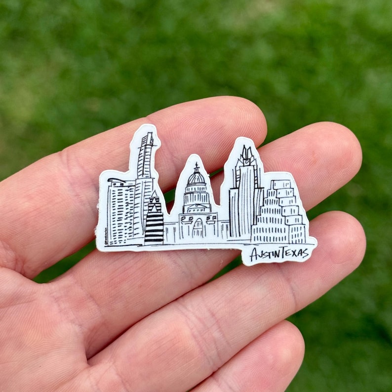 May include: A white sticker featuring a black and white illustration of the Austin, Texas skyline. The sticker includes the text "Austin Texas" at the bottom. The design depicts various buildings and landmarks.