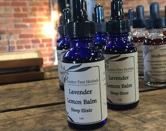 May include: Two small blue glass bottles with droppers filled with a clear liquid. The bottles have white labels with black text that reads "Linden Tree Herbals Lavender Lemon Balm Sleep Elixir 1 oz".