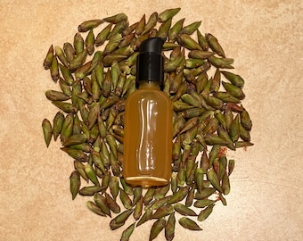 May include: A clear glass bottle with a black pump top filled with a light yellow liquid. The bottle is surrounded by small green buds.