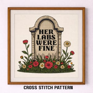 May include: Cross-stitch pattern framed in a wooden frame. The artwork features a tombstone with the text "HER LABS WERE FINE" surrounded by red, white, and yellow flowers and green foliage. The words "CROSS STITCH PATTERN" are at the bottom.