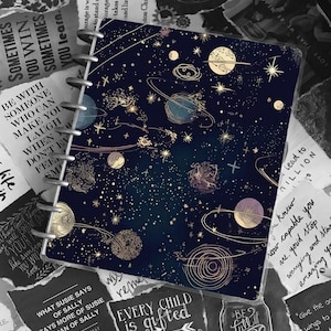May include: A dark blue planner with a gold and white celestial pattern. The planner has a gold ring binding and the words "Every child is gifted" and "They just unwrap their packages at different times" are printed on the cover.