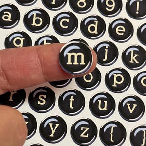May include: Black and white typewriter key stickers with letters and numbers. The stickers are round and have a glossy finish. The letter "m" is highlighted.