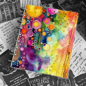 May include: A colourful notebook with a watercolour design of overlapping circles in shades of yellow, pink, purple, and blue. The notebook has a spiral binding and is surrounded by torn pieces of paper with inspirational quotes, including "Every child is gifted" and "Be full of joy".